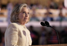 Hillary Clinton Ignites Firestorm Person standing at podium with microphone speaking indoors