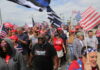 Crowd of people at a political rally holding flags and wearing hats