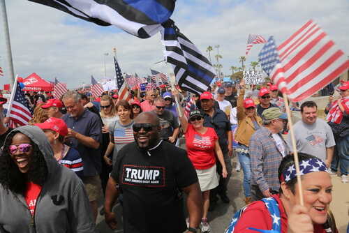 Crowd of people at a political rally holding flags and wearing hats