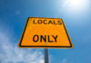A yellow road sign that reads 'LOCALS ONLY' against a blue sky