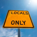 A yellow road sign that reads 'LOCALS ONLY' against a blue sky