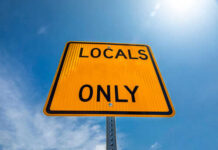 A yellow road sign that reads 'LOCALS ONLY' against a blue sky