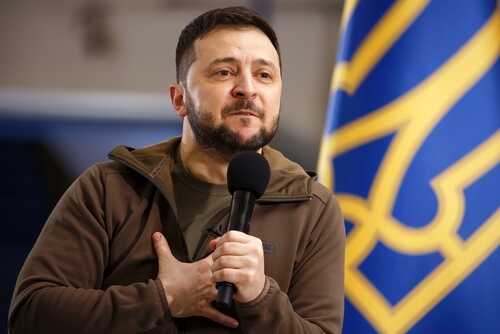 A political leader speaking passionately into a microphone with a national flag in the background