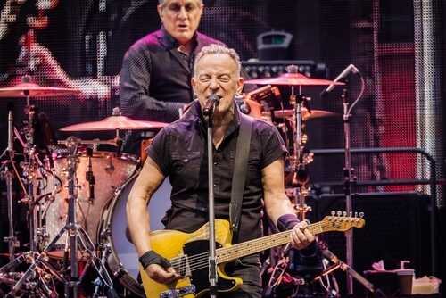 A guitarist performing on stage with a drummer in the background