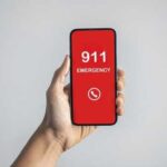 Hand holding a smartphone displaying an emergency call screen with 911