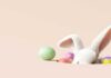 A cute white bunny peeking out from behind colorful Easter eggs