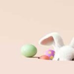 A cute white bunny peeking out from behind colorful Easter eggs