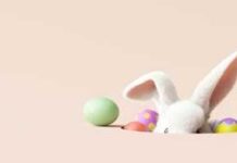 A cute white bunny peeking out from behind colorful Easter eggs