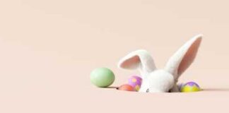 A cute white bunny peeking out from behind colorful Easter eggs
