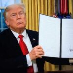 A man in a suit holding a signed document in an office setting
