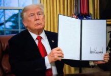 A man in a suit holding a signed document in an office setting