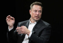 Court Smacks Down Musk Power Grab Man in suit speaking, black background, gesturing with hands.