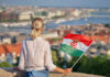 A woman holding a Hungarian flag while overlooking a cityscape