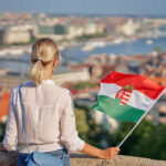 A woman holding a Hungarian flag while overlooking a cityscape