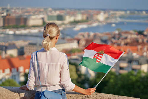 A woman holding a Hungarian flag while overlooking a cityscape
