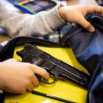 A person reaching into a backpack that contains a handgun