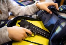 A person reaching into a backpack that contains a handgun