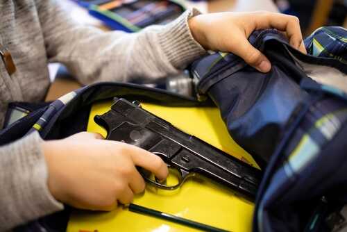 shutterstock_2074388671.jpg A person reaching into a backpack that contains a handgun