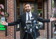 SOCIALIST TAKEOVER: NYC Financial Capital Under SIEGE Man in a suit speaking at a press conference with microphones in front of him