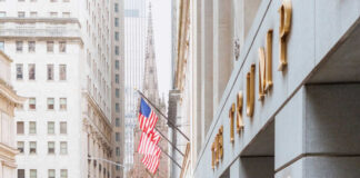 American flag on building corner with spire in background.
