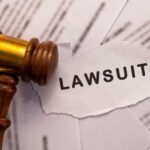 A wooden gavel next to a torn paper with the word 'LAWSUIT'