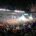 A large crowd celebrating at a football game with fireworks in the background
