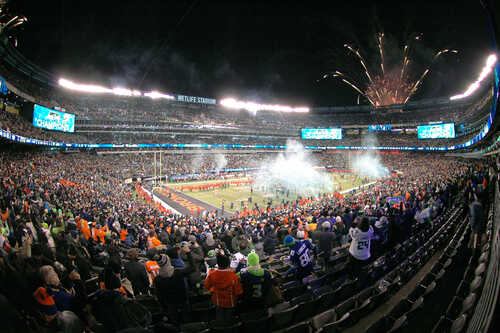 A large crowd celebrating at a football game with fireworks in the background
