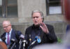 Man speaking at press conference with microphones.