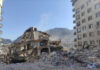 Aid Crawls In, Chaos Erupts Collapsed building surrounded by debris and mountains