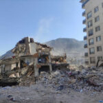 Collapsed building surrounded by debris and mountains