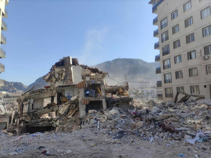Collapsed building surrounded by debris and mountains
