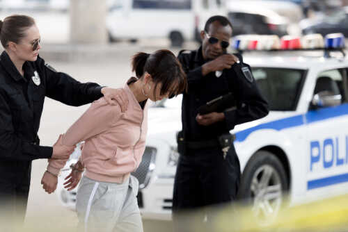 Policewoman,Holding,Arrested,Young,Woman,While,Her,Partner,Talking,On Police officers arresting a suspect in an urban environment