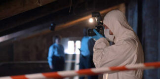 Forensic investigator in protective gear photographing a crime scene in an attic