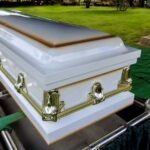 A white coffin placed on a green cloth at a cemetery