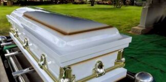A white coffin placed on a green cloth at a cemetery