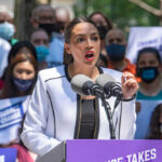 Person speaking at a public event with crowd.