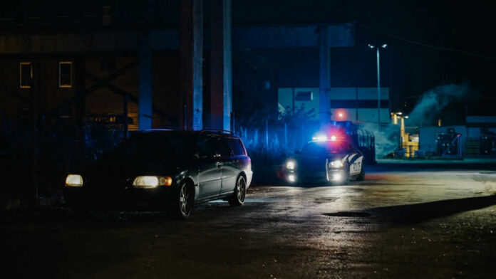 2232056193 A police car with flashing lights parked next to a dark vehicle in a dimly lit urban area