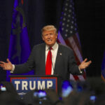 Man speaking at a podium with American flags.