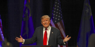 Man speaking at a podium with American flags.