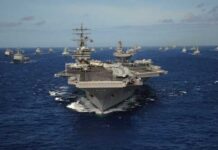 An aircraft carrier surrounded by a fleet of naval ships in the ocean