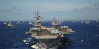 An aircraft carrier surrounded by a fleet of naval ships in the ocean