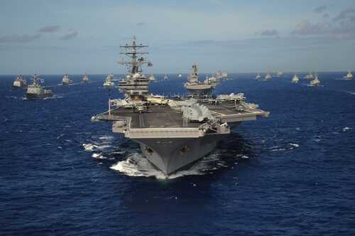 An aircraft carrier surrounded by a fleet of naval ships in the ocean
