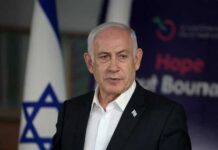 A political leader speaking at a press conference with the Israeli flag in the background