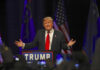 Man speaking at a podium with American flags.