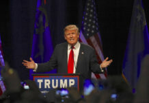 Trump’s Economic D‑Day Slams Iran Man speaking at a podium with American flags.