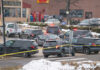 Manhunt After Veteran Cop Found Dead Multiple police vehicles at a scene with caution tape and emergency lights activated