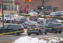 Manhunt After Veteran Cop Found Dead Multiple police vehicles at a scene with caution tape and emergency lights activated