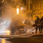 Firefighters extinguishing a car fire on a city street at night