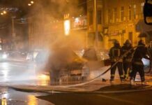 Firefighters extinguishing a car fire on a city street at night