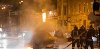 Firefighters extinguishing a car fire on a city street at night